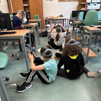 Uczniowie w goglach VR siedząc bezpiecznie na podłodze wspinają się w wirtualnej rzeczywistości po fasoli.