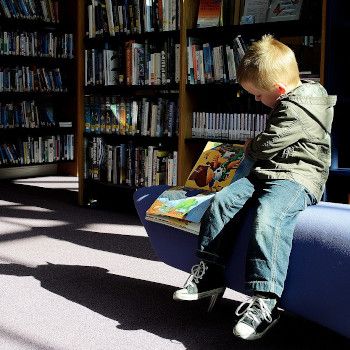 Chłopiec siedzi na niebieskiej pufie w księgarni i przegląda książeczkę.