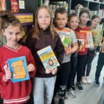 3_Mistrzowie_jezyka_ojczystego_i_ortografii._Uczniowie_stoja_w_bibliotece_i_trzymaja_w_rekach_ksiazki